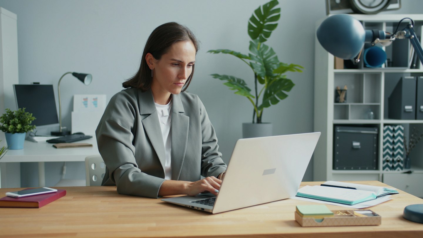 Woman works on her laptop at a desk with plants.