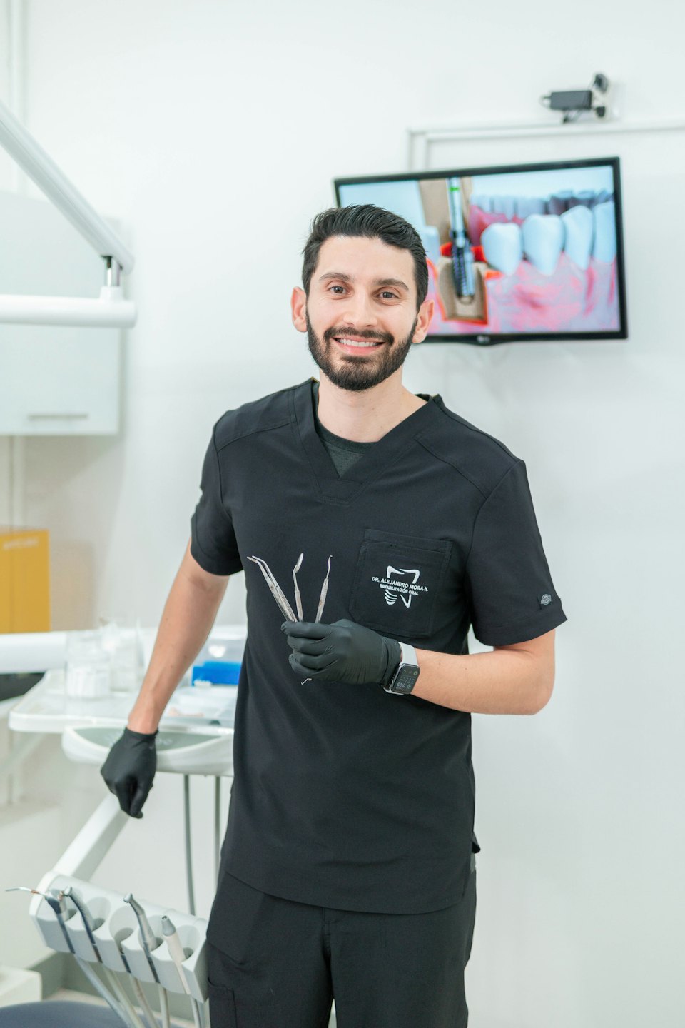 Hispanic dentist in scrubs holds dental tools in a bright office.